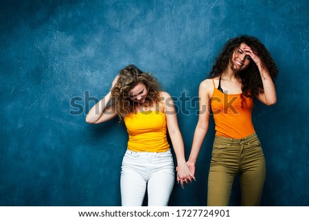 young pretty teenage girls friends with blond and brunette curly hair posing cheerful on blue background, lifestyle people concept