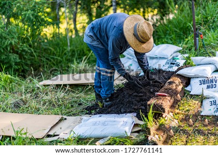 Gardener spreading compost as he prepares a new no dig vegetable garden. Permaculture gardening principles. Self sufficiency, organic food, sustainability. Rural setting. Outdoors.  Royalty-Free Stock Photo #1727761141
