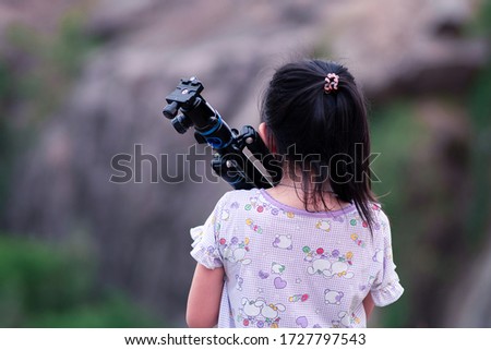 Back of little child girl carrying out tripod at green natural background.