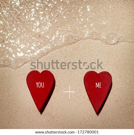 two romantic  red valentine's hearts laying on the wet sand on the beach with text "you and me" as the symbol of love forever.