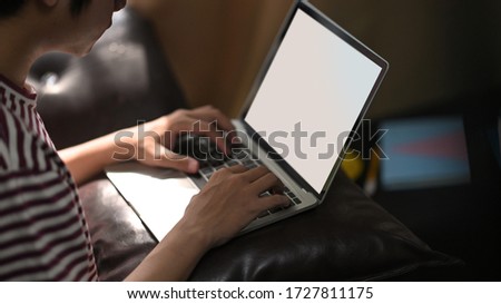 Cropped image of creative man typing on white empty screen while sitting at leather couch over comfortable living room as background.