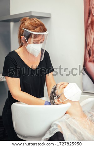 Hairdresser with mask and gloves washing the client's hair with soap. Reopening with security measures of Hairdressers in the Covid-19 pandemic Royalty-Free Stock Photo #1727825950