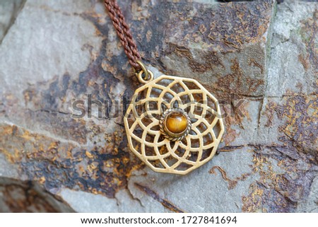 Brass pendant with natural tyger eye gemstone on rocky background