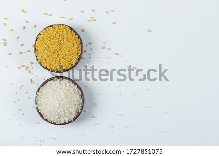 Raw round rice with a bowl of dry bulgur in a clay bowl on white background, flat lay.