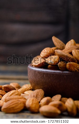 Peeled almonds in a clay plate on stone tile and wooden background. close-up.