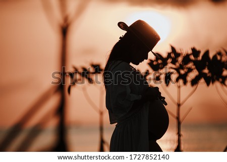 Silhouette of beautiful asian young pregnant woman with white dress is standing by the sea at Phangan island in evening time. Selective focus and split color.