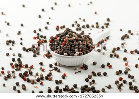 Mixed peppercorns in a white scoop side view on spicy and white background