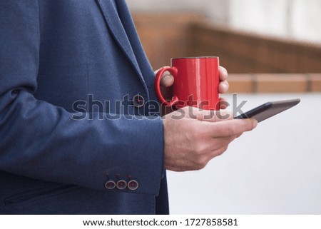 man in suit using digital tablet while having cup of coffee