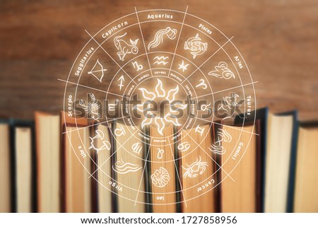 Old books and illustration of zodiac wheel with astrological signs on wooden background