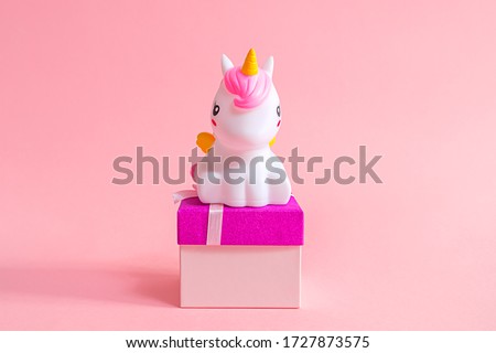 A cute cartoon unicorn figurine stands on a gift box on a pink background. Gifts for the girl on a holiday: birthday, Christmas, International Women's Day, Valentine's Day