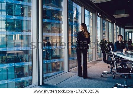 Back view of confident female in elegant suit standing near window in office with panoramic view on business buildings pondering about career, prosperous woman in formal outfit thinking about job Royalty-Free Stock Photo #1727882536