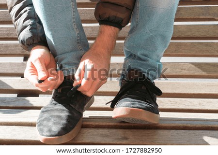 man tying his shoelaces on top of a street bench