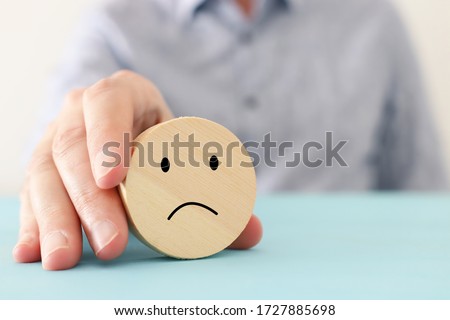 male hand holding wooden cube with sad face. concept of anxiety, stress or sad emotions