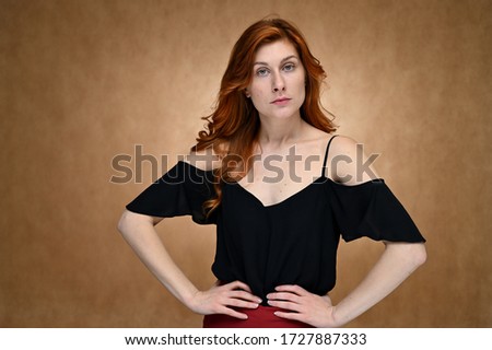 Model actress shows different emotions. Studio photo portrait of a caucasian young woman in a black blouse with long red hair on a beige background.