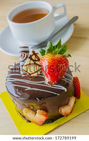 Chocolate cake with strawberry on top & tea white cup on the wood table