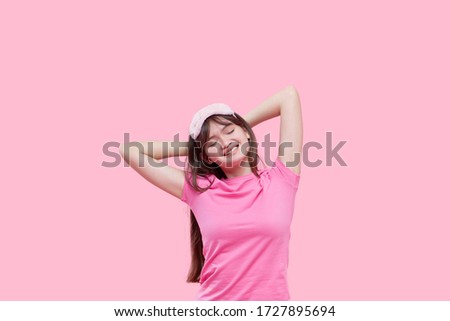 Young asian woman in sleeping eye mask yawning and holding alarm clock isolated on pink. Sleepless night