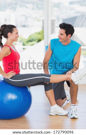 Smiling male trainer helping woman with her exercises at a bright gym