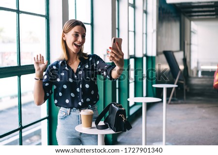 Overjoyed caucasian blonde woman in trendy wear posing for selfie holding mobile phone spending coffee break in cafe, smiling successful female influencer share good news via smartphone video in vlog