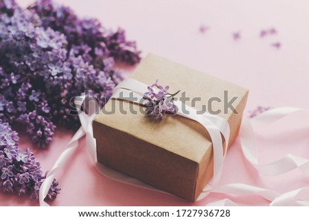Lilac flowers and gift box on pink background. Stylish floral greeting card. Purple lilac flowers bouquet, craft present box with ribbon on pink paper. Happy mothers day