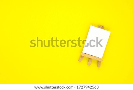 drawing equipment, wooden easel with a blank canvas isolated on a yellow background. background for designers with space for text