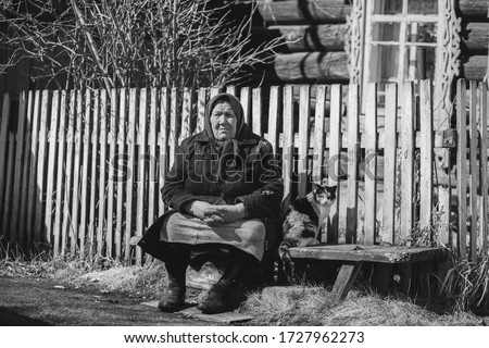 
Grandmother sits on a bench near the house, grandmother with a cat, old age, retirement, Russian village. Russian pensioner, pension, village life. black and white Royalty-Free Stock Photo #1727962273