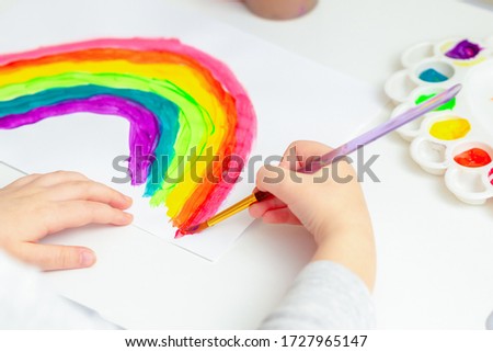Close up of hand of kid with painted rainbow on white paper during the Covid-19 quarantine at home. Children's creativity.