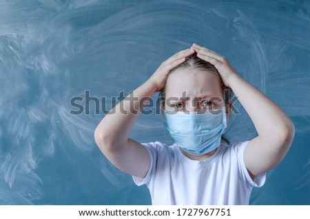 Girl in a medical mask on the background of a school blackboard. Emotions of anger on the face. Selective focus, copy space
