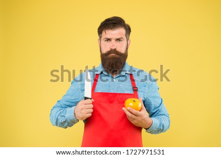 brutal cook cut tomato. man in apron with long beard. handsome confident guy cooking vegetable food. healthy eating and diet. hunting on vitamins. bearded chef wearing red apron.