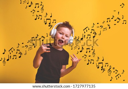 Cool little boy in headphones singing a song with music notes drawn on wall. Isolated on yellow background. 
