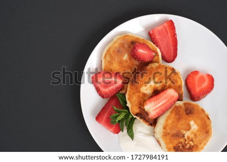 Russian and Ukrainian cuisine. Breakfast. Cottage cheese pancakes. Cheesecakes with fresh strawberries, mint and sour cream sauce in white plate on light grey background. Copy space close-up top view