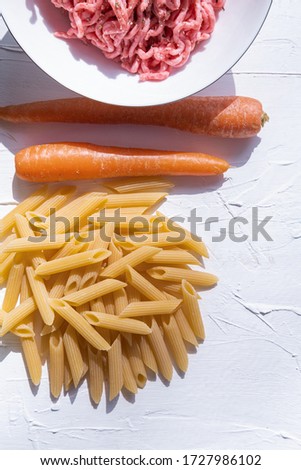 Carrot, macaroni and minced meat on white background. Vetical picture.