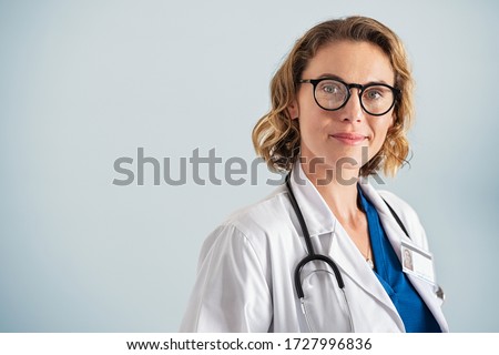 Portrait of happy mid adult smiling doctor looking at camera. Happy beautiful mature pediatrician standing over blue background with copy space. Reliable general practitioner woman with stethoscope.