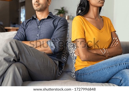 Middle eastern couple sitting back to back after a fight. Young indian couple in fight with arms crossed sitting on couch after quarrel at home. Young mixed race woman and his boyfriend sitting angry. Royalty-Free Stock Photo #1727996848
