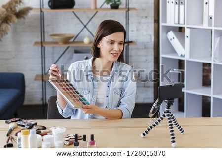 Young female blogger recording a tutorial video for her beauty blog about cosmetics.Vlogger testing eyeshadow and broadcast live video to social network at home.Blogging, videoblog, makeup concept.