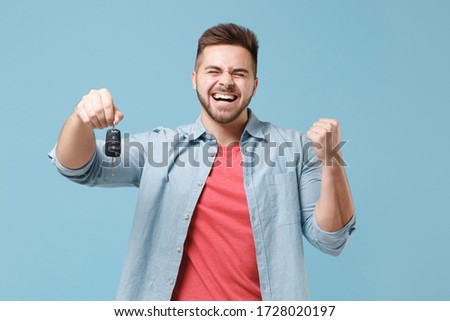 Happy young bearded guy 20s in casual shirt posing isolated on pastel blue wall background studio portrait. People emotions lifestyle concept. Mock up copy space. Hold car keys, doing winner gesture