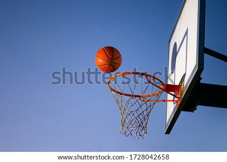 Street basketball ball falling into the hoop. Close up of orange ball above the hoop net with blue sky in the background. Concept of success, scoring points and winning. Copy space Royalty-Free Stock Photo #1728042658
