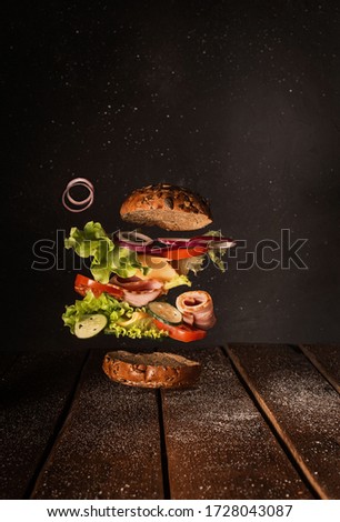 Delicious burger with flying ingredients isolated on black background. Food levitation concept. High resolution image