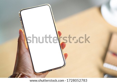 Close up of hand holding smartphone in co working space with notebook, pencils, rubber, clips, cup of coffee, eyeglasses put on white background. Flat lay, top view.