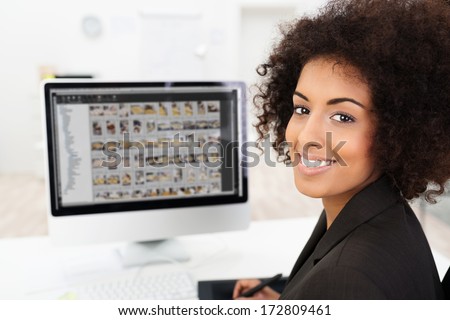 Smiling African American businesswoman editing photographs visible on her computer screen as she turns to smile at the camera