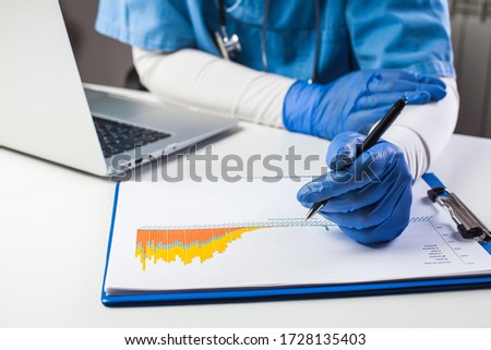 Doctor wearing protective gloves analyzing COVID-19 info data,Coronavirus global pandemic outbreak crisis,stats showing rising number of infected patients,death toll and mortality rate,easing measures Royalty-Free Stock Photo #1728135403