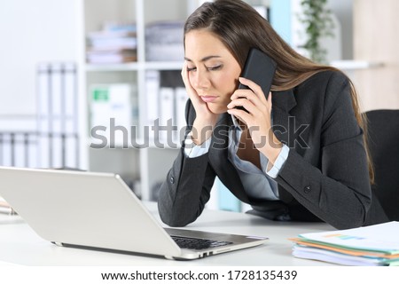 Bored executive calling on smart phone waiting on hold sitting on her desk at the office