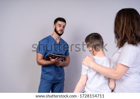 Slender pediatrician with a beard holding a folder and looking at the mother and son, the concept of consultation and treatment.