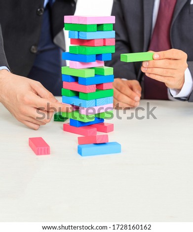 Colorful blocks tower on a white office desk. Two men playing a board game. Business strategy, risk, construction concept