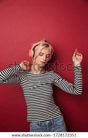 Image of nice happy woman with headphones listening music and dancing isolated over red background