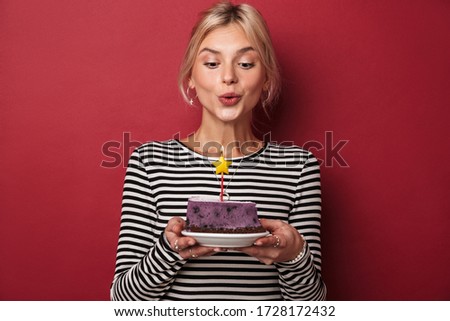 Image of nice happy woman in striped sweatshirt holding cake with candle isolated over red background