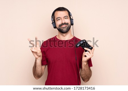 Man playing with a video game controller over isolated wall showing victory sign with both hands