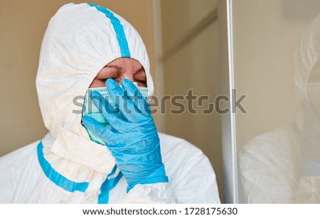 Tired doctor in protective clothing yawning holds hand in front of face in clinic during coronavirus pandemic