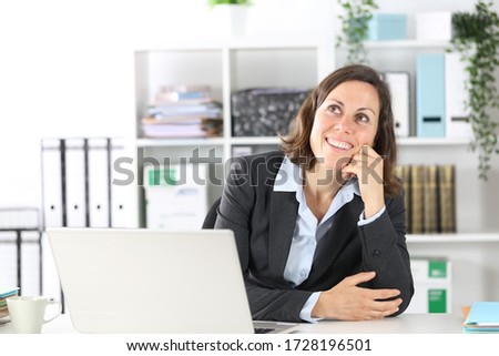 Pensive executive lady thinking looking up imagining sitting on a desk at office