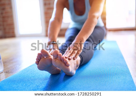 Middle age beautiful sportwoman sitting on mat practicing yoga doing seated forward fold pose at gym