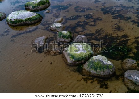 Stones in the calm shallow waters. Little moss on rocks. No reflection of the water - can see through. Clear water. Can see bottom of the water. Slow shutter speed photography. Sea side in Estonia.